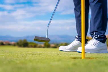 Golf sopasıyla yeşile vuruyor. Top delikte. Golf oynayan adam.