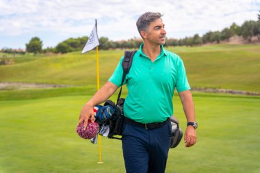 Beyazlı profesyonel bir golf oyuncusu golf sahasında, yeşil bayrağın yanında.