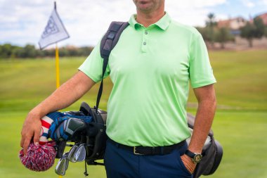 Bir erkek golfçü çim yolunda çantalarla yürüyor.