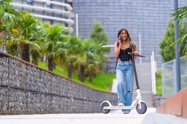 Young woman in the city with an electric scooter talking on the phone, sustainable transport