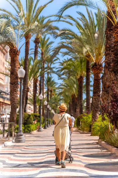 City of Alicante. An elderly lady with her grandson on the Las Olas footbridge with beautiful palm trees on the coast