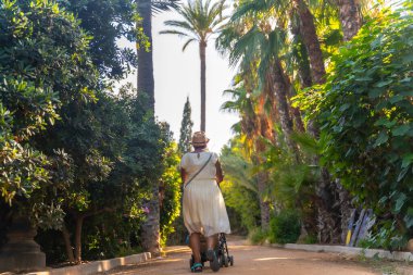 Alicante şehrindeki El Palmeral parkında torunuyla yürüyen bir büyükanne.