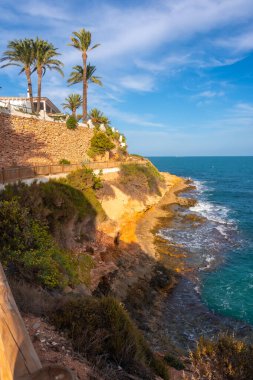 Yazın Cabo Roig 'de Caleta sahilinin yanındaki güzel kırmızı sahil ve palmiye ağaçları. Alicante