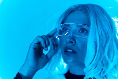 Gelecekçi kavram, geleceğin gözlüklü genç bir kadın mavi arka planda, sanal gerçeklikte