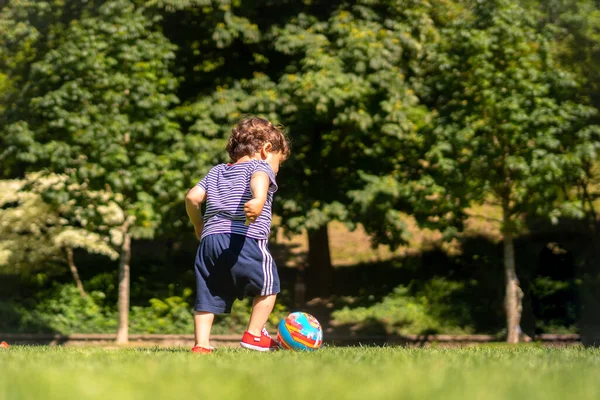Boy playing ball in a park. First step and already kicking the ball, having fun
