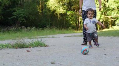 Parkta annesiyle top oynayan bir çocuk. İlk adım ve şimdiden topa vuruyorsun, eğleniyorsun.