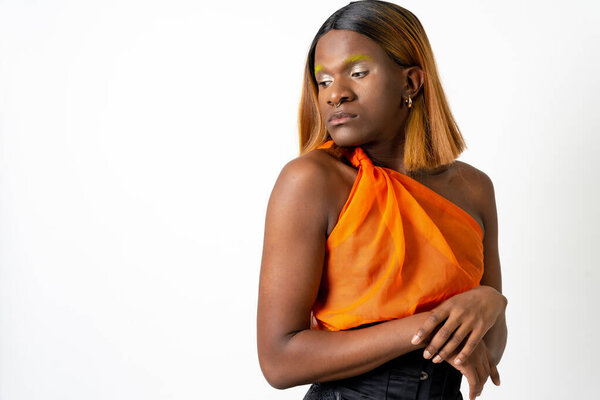 Black ethnic man in a studio, LGTBI concept, portrait wearing an orange and black dress and with a wig