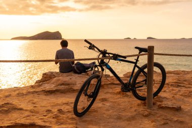 İbiza adasındaki Cala Comte plajında bisiklet süren bir turist. Gün batımı. Balearic
