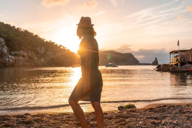 İbiza 'da gün batımında Benirras plajına bakan genç bir kadın. tatil kavramı