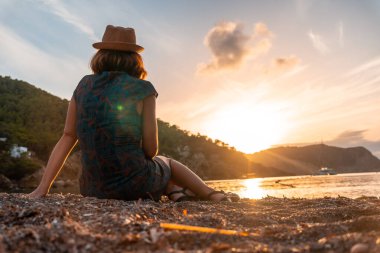 Gün batımında Ibiza 'da Benirras plajına bakan genç bir kadın. tatil kavramı