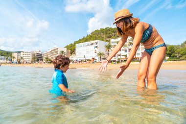 Anne oğluyla denizde eğleniyor, İbiza plajı San Vicente plajında tatilde, Balearic.