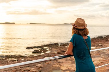 San Antonio Abad, İbiza Adası 'ndaki Paseo de Poniente' de gün batımına bakan genç bir kadın. Balearic