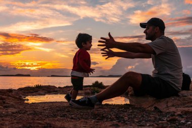 Ibiza 'da gün batımında, genç baba deniz kenarında oğluna sarılıyor, San Antonio Abad.