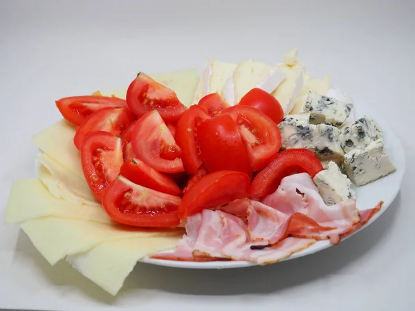 Plate with bacon, tomato, cheese, blue cheese and tomatoes on a white background