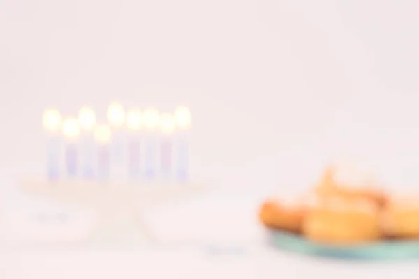 Rozostřené rozmazané pozadí s Chanuka dovolená scéna s modrým osvětlením svíčky a tradice Chanuka koblihy sufganiyot proti bílému pozadí — Stock fotografie