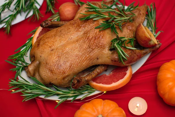 Anatra natalizia o del Ringraziamento cotta per la tradizionale cena festiva con mele, rosmarino, pompelmi sulla tavola rossa di Natale decorata con zucche e candele. Focus selettivo — Foto Stock