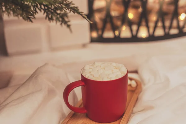 Cozy vibes scene with a cup of hot drink with white marshmallows in front of fireplace. Selective focus. Cozy atmosphere during winter holidays concept — Stock Photo, Image