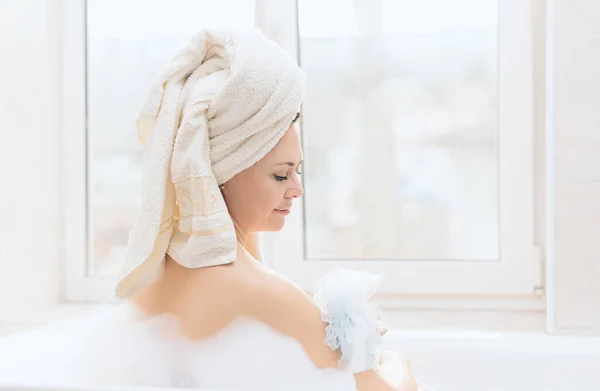 Genç bir kadın pencerenin yanında köpüklü bir banyo yapar. Kişisel hijyen, sağlık konsepti — Stok fotoğraf