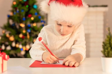 Kırmızı Noel Baba şapkalı çocuk Noel Baba 'ya mektup yazıyor. Noel ya da yeni yıl konsepti. Xmas zamanı. Seçici odak