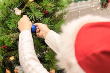 Kırmızı Noel Baba şapkalı çocuk Noel ağacını yakından süslüyor. Xmas ya da yeni yıl konsepti. Seçici odak