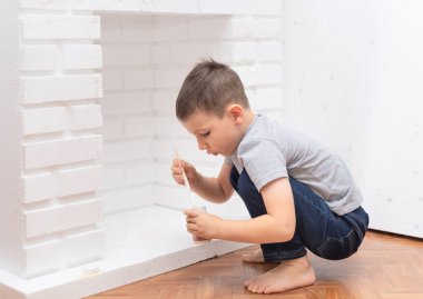 Çocuk yere oturur ve beyaz boya kebabıyla dekoratif bir şömine boyar. Ev geliştirme, DIY konsepti. Seçici odak
