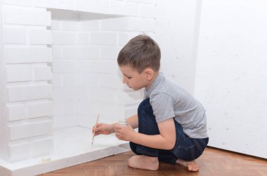 Çocuk yere oturur ve beyaz boya kebabıyla dekoratif bir şömine boyar. Ev geliştirme, DIY konsepti. Seçici odak