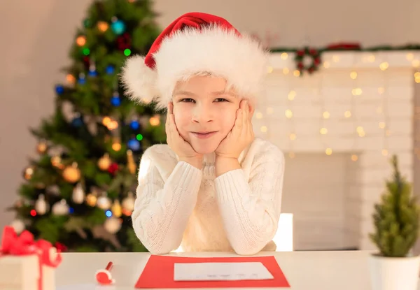 Child boy in red Santa hat writing a letter to Santa Claus. Christmas or New Year cozy holidays concept. Xmas time. Selective focus — Stock Photo, Image