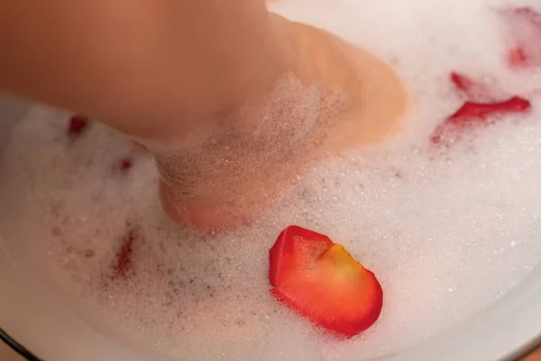 Woman feet in water with soap foam and rose petals close up with selective focus. Spa treatment for dry feet skin. Homemade bath soak for female feet and hand. Skin care concept. Luxurious lifestyle — Φωτογραφία Αρχείου