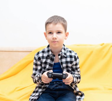 Çek gömlekli çocuk elinde siyah joystick ile kanepede oturmuş video oyunu oynuyor. Ev konseptinde video oyunları oynamak