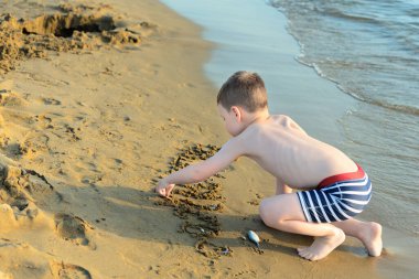Mutlu çocuk deniz kıyısında kumla oynuyor. Yaz ve seyahat konsepti