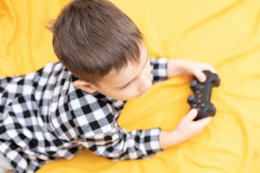 Kanepede elinde siyah joystick ile video oyunu oynayan kareli tişörtlü çocuk. Ev konseptinde video oyunları oynamak
