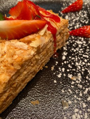 Siyah bir tabakta taze çilekli Napolyon keki. Pudra şekerli. Seçici bir odak ile yakın plan.