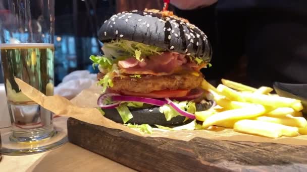 Mann in Handschuhen isst schwarzen Burger aus nächster Nähe. Food Truck und Streetfood-Konzept. Zeitlupe — Stockvideo