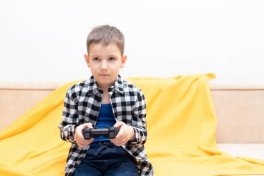 Çek gömlekli çocuk elinde siyah joystick ile kanepede oturmuş video oyunu oynuyor. Ev konseptinde video oyunları oynamak
