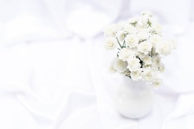 Beyaz arkaplanda beyaz vazodaki beyaz çiçekler ve fotokopi alanı. Seçici odaklı üst görünüm. Selamlama veya davet kartı