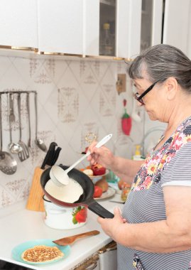 Kıdemli kadın lezzetli kahvaltı için sabah mutfakta lezzetli gözlemeler hazırlar. Maslenitsa kavramı. Geleneksel Rus yemekleri. Evde büyük krepler pişiriyorum.