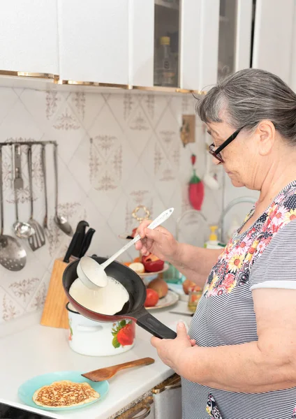Senior woman prepares delicious pancakes in the kitchen in the morning for tasty breakfast. Maslenitsa concept. Russian traditional food. Cooking big crepes at home — Stock Photo, Image