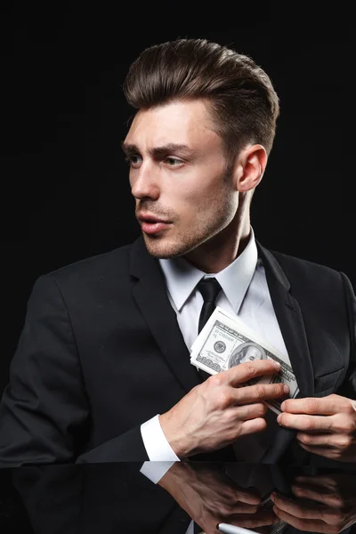 Pohledný mladý muž v obleku na tmavém pozadí s penězi — Stock fotografie