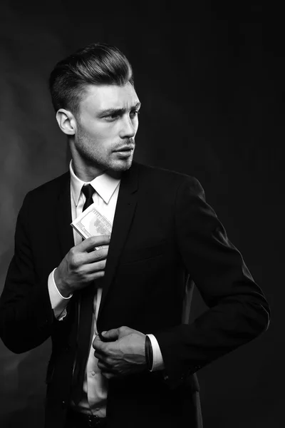 Hombre joven guapo en traje sobre fondo oscuro con dinero —  Fotos de Stock