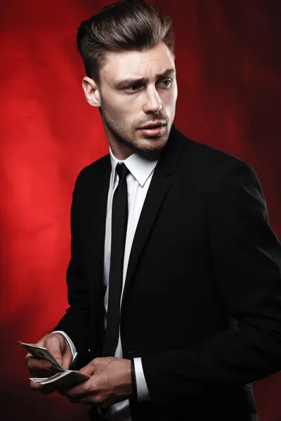 Handsome young man in suit on dark background with money — Stock Photo, Image