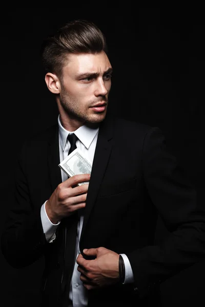 Pohledný mladý muž v obleku na tmavém pozadí s penězi — Stock fotografie