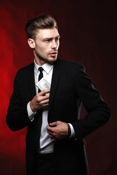 Handsome young man in suit on dark background with money — Stock Photo, Image