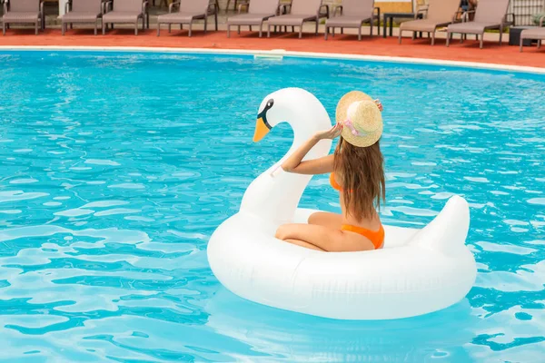Young Girl Orange Bathing Suit Swims Pool Inflatable White Swan lizenzfreie Stockfotos