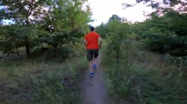 Parlak tişörtlü bir adam orman yolunda yokuş yukarı koşar. Arkadan bak. Fitness konsepti.