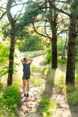 Genç bir kadın orman yolunda yürüyor. Yaz tatili.