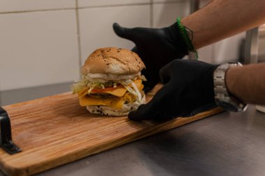 A man is preparing a big double burger with fries in the kitchen.