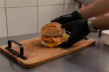 A man is preparing a big double burger with fries in the kitchen.
