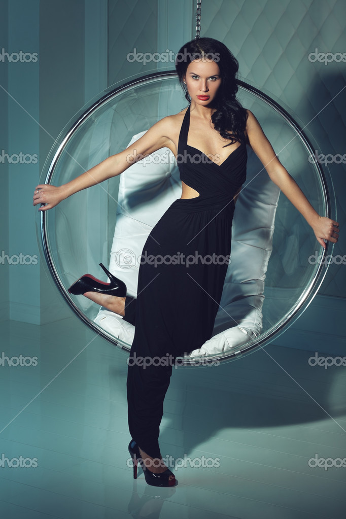 Sexual Girl With Dark Hairs Stands Near A Round Chair