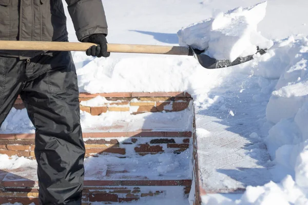 De conciërge reinigt het gebied van de sneeuw, houdt een schop in zijn handen, veel sneeuwverschuivingen — Stockfoto