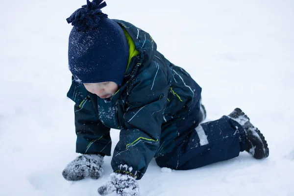 Tulumlu ve eldivenli küçük bir çocuk kışın karda yakın planda oynar. — Stok fotoğraf